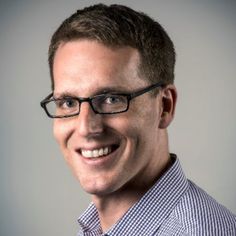 a man with glasses smiling at the camera while wearing a checkered shirt and tie