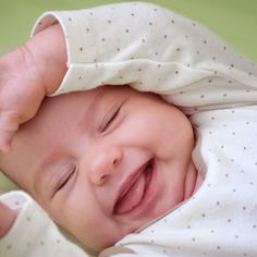 a close up of a baby smiling with its eyes closed and hands on top of his head