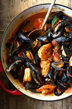 a red pot filled with seafood and mussels on top of a wooden table