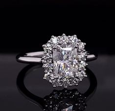 an engagement ring with a cushion cut diamond surrounded by small round brilliant diamonds on a black background