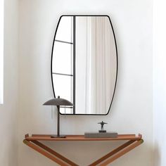 a mirror sitting on top of a wooden shelf next to a lamp and table with a lamp