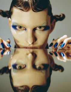 a man with blue makeup holding his hands up to his face and reflecting in the mirror