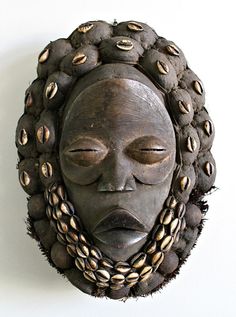 a wooden mask with many beads around it's neck and face, hanging on a wall