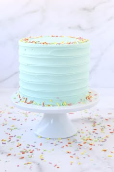 a frosted cake with sprinkles on a white pedestal and marble background