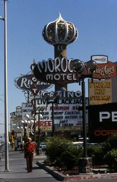 a woman walking down the street in front of motels and other signs on a sunny day