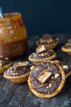 chocolate covered cookies with nuts and caramel on a table next to a jar of peanut butter