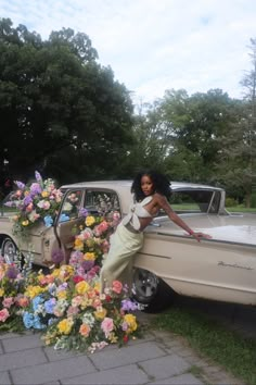 a woman leaning on the back of a car with flowers in front of her,