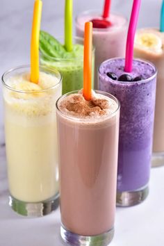 four different types of smoothies are lined up in glass cups with colorful straws sticking out of them