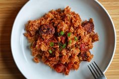 a white plate topped with meat and rice on top of a wooden table next to a fork