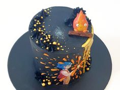 a black cake with an orange and yellow decoration on it's top, sitting on a blue plate