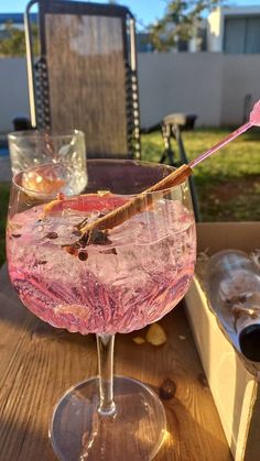 a pink drink in a wine glass sitting on a wooden table with an arrow sticking out of it