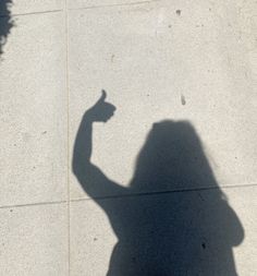 the shadow of a person holding a cell phone up in the air with one hand