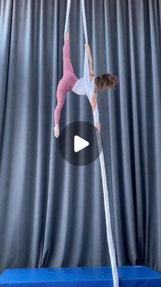 a woman standing on top of a pole in front of a blue curtain and holding onto the pole