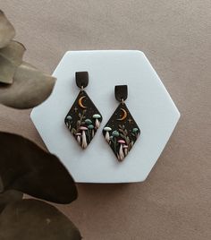 a pair of black and white earrings sitting on top of a table next to a plant