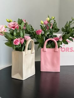 two vases with pink flowers and green leaves on a table next to a sign