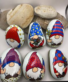 six painted rocks with gnomes on them next to some rocks and a rock in the background