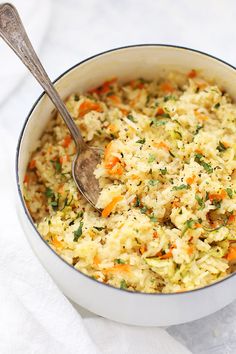 a bowl filled with rice and carrots on top of a white cloth next to a wooden spoon