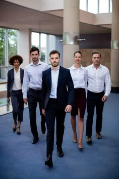 a group of men and women walking down a blue carpeted hallway in front of large windows