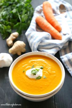 a white bowl filled with carrot soup and topped with sour cream next to fresh vegetables