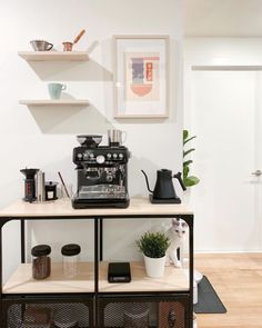 a coffee machine sitting on top of a wooden table next to a shelf filled with cups and saucers