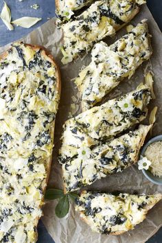 slices of bread topped with cheese and herbs on top of wax paper next to garlic