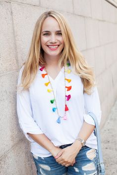 a woman standing next to a wall with her hands in her pockets and smiling at the camera