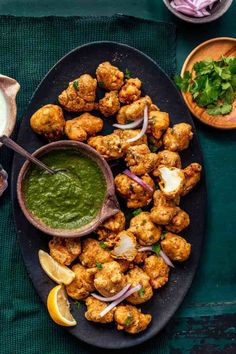 a black plate topped with tater tots covered in green sauce and garnished with cilantro