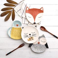 three plates with animals on them sitting next to spoons and utensils in front of leaves