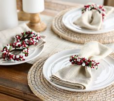 the table is set with white plates, napkins and red berries on top of them