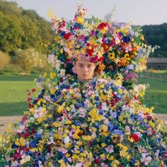 a woman with flowers on her head is standing in front of a large pile of flowers