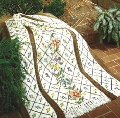 a white quilt sitting on top of a brick floor next to a potted plant