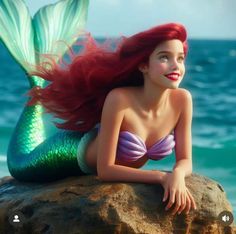 a mermaid with red hair laying on top of a rock next to the ocean and smiling