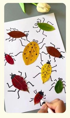 a child's hand is drawing leaves on a paper with ladybugs in the background