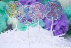 three lollipops with mermaid designs on them sitting on top of a cake