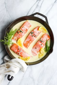 salmon with lemon and dill in a skillet on a marble countertop next to a white towel