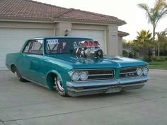 an old blue car parked in front of a garage with two engines on the hood