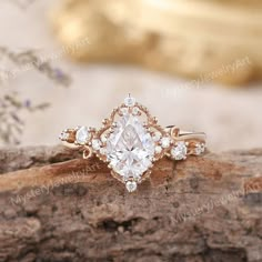 an engagement ring with a pear shaped diamond surrounded by smaller round brilliant cut diamonds on a piece of wood