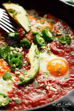 an egg and avocado on top of tomato sauce in a skillet with a fork