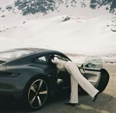 a woman standing next to a car on the side of a road in front of snow covered mountains