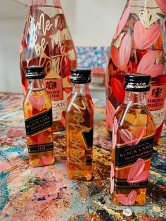 three bottles filled with liquid sitting on top of a painting covered table next to each other