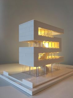 a model of a white building with yellow lights on the windows and in front of it