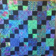 a blue and green patchwork quilt hanging on a wall