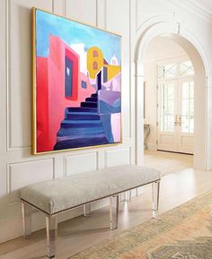 a painting hanging on the wall above a bench in a room with white walls and wooden floors