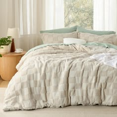 an unmade bed in a bedroom with white curtains and green plants on the window sill