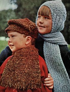 two children wearing knitted hats and scarves, one boy is holding the other