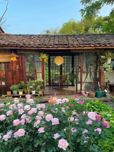 a garden with lots of pink flowers in front of a wooden building and patio area