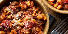 two bowls filled with pasta and sauce on top of a wooden table next to silverware