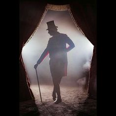 a man with a top hat and cane standing in front of a stage curtain holding a cane