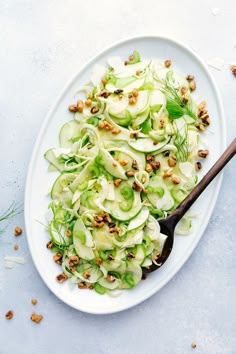 a white plate topped with cucumber and nuts next to a wooden spoon on top of a table