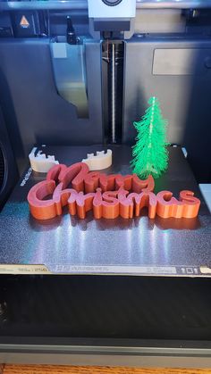 a 3d printing machine with the word christmas spelled out in red letters and a green tree on top